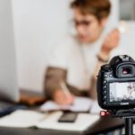 Photography Career - Unrecognizable blurred lady working at table in modern office against photo camera placed on tripod