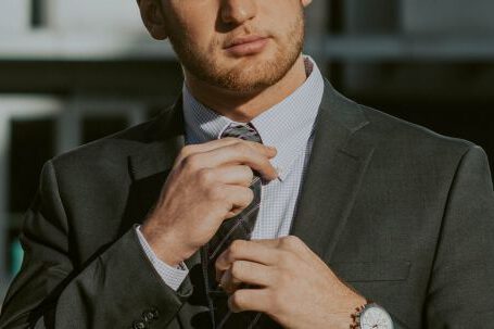 Finance Careers - Serious confident male entrepreneur wearing classy suit and wristwatch holding tie while thoughtfully looking away