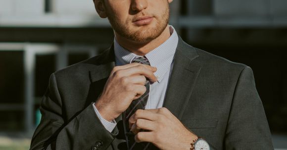 Finance Careers - Serious confident male entrepreneur wearing classy suit and wristwatch holding tie while thoughtfully looking away