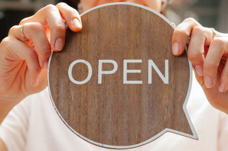 Hospitality Careers - Happy woman showing wooden signboard saying open