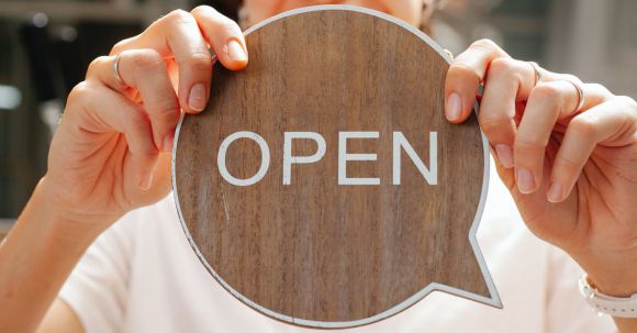 Hospitality Careers - Happy woman showing wooden signboard saying open