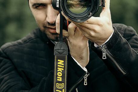 Career Exploration - Concentrated male photographer in casual clothes looking through objective lens of camera while taking photo on nature with blurred background