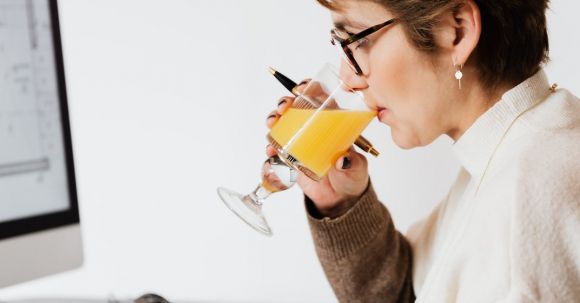 Nutrition Careers - Focused female drinking refreshing juice while working at table in office
