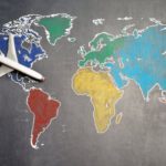 Internship Guide - Top view of crop anonymous person holding toy airplane on colorful world map drawn on chalkboard