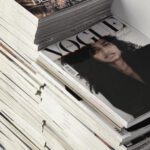 Publishing Internship - High angle many fashion magazines stacked on floor against white brick wall in studio