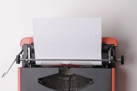Journalism Careers - From above crop person using vintage black and red typewriter with white blank sheet of paper against white background